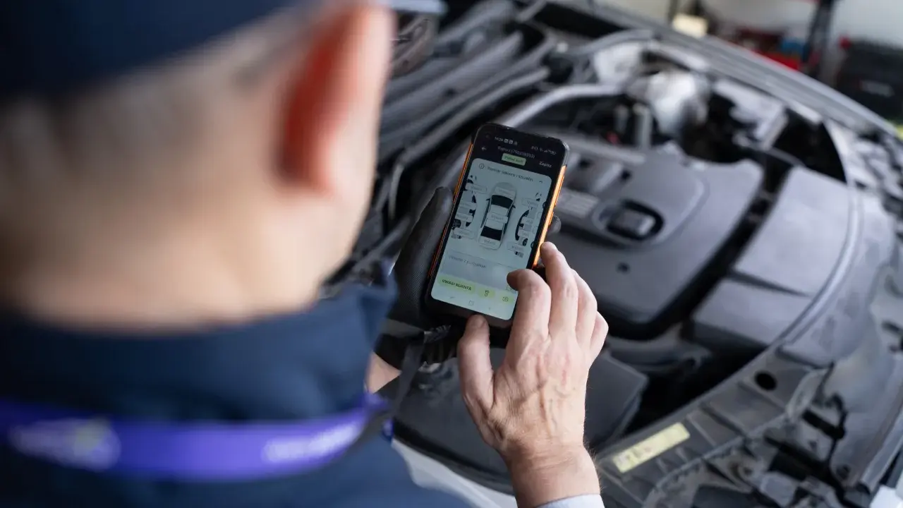 Mechanik sprawdza kody samochodowe na telefonie, analizując raport z pomiaru lakieru i szczelin.
