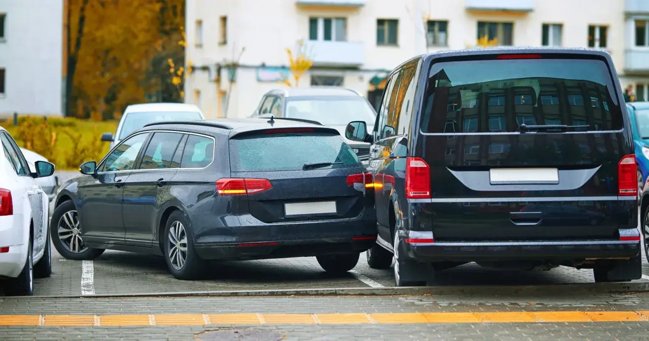 Ciemny kombi zaparkowany zbyt blisko drugiego samochodu, ledwo mieszcząc się na miejscu parkingowym.