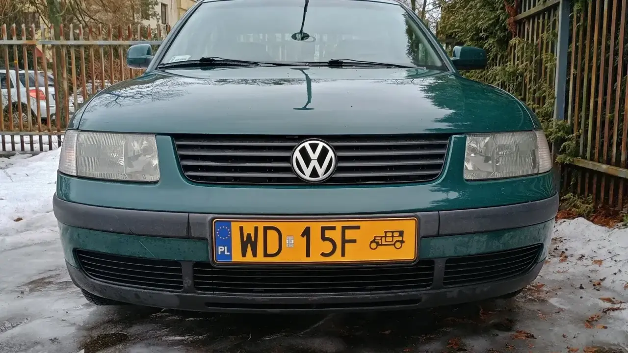 Zielony Volkswagen z żółtą tablicą rejestracyjną na tle płotu i śniegu.