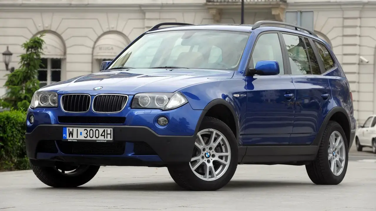 Niebieskie BMW E83, SUV, stoi przed budynkiem z łukami.