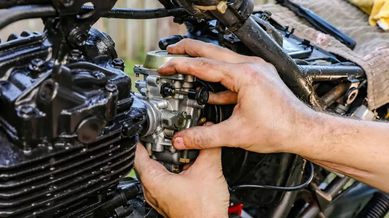 Ręce mechanika regulują gaźnik motocykla, pokazując, jak działa ssanie.