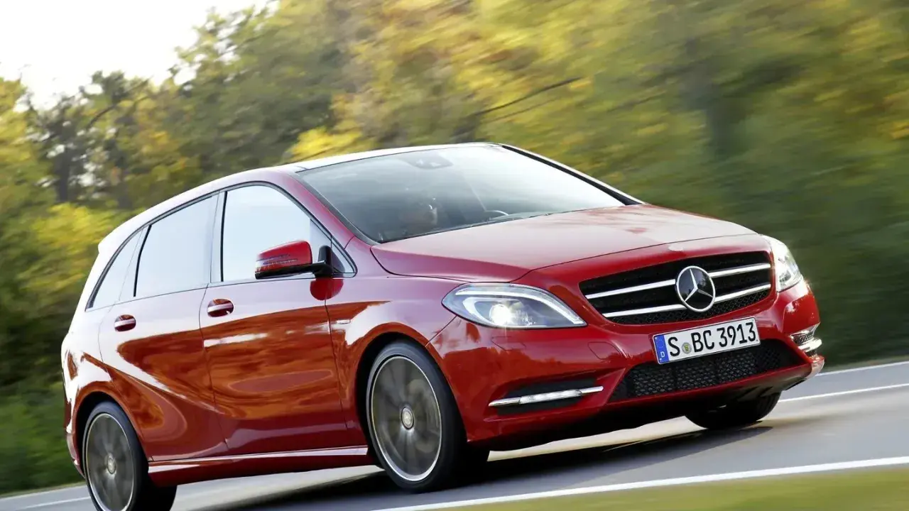 Czerwony Mercedes Klasy B w ruchu, z rozmytym tłem drzew i drogi.