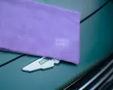 Fioletowa mikrofibra z logo Work Stuff na masce zielonego samochodu. Idealna do pielęgnacji lakieru.