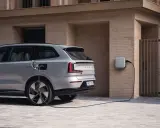 Srebrny, duży SUV Volvo EX90 podłączony do ładowarki ściennej. Nowoczesny design i ekologiczna energia.