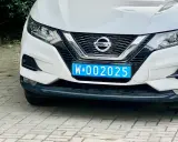 Biały Nissan z niebieską tablicą rejestracyjną W-002025, wskazującą na dyplomatyczne tablice rejestracyjne.