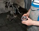 Mechanik trzyma nowe łożysko koła, przygotowując się do wymiany. Tak sprawdzić łożysko w kole.