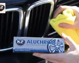 Ręce polerują chromowaną atrapę chłodnicy samochodu, używając żółtej ściereczki i pasty K2 Aluchrom.