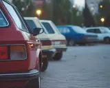 Rząd klasycznych, bezawaryjnych aut na parkingu. Czerwony klasyk z tyłu, za nim żółty, niebieski i biały.