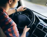 Mężczyzna w koszuli w kratę trzyma kierownicę, czując delikatne drgania kierownicy podczas jazdy.