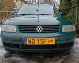 Zielony Volkswagen z żółtą tablicą rejestracyjną na tle płotu i śniegu.
