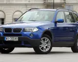 Niebieskie BMW E83, SUV, stoi przed budynkiem z łukami.