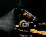 Rękawiczka w czarnej rękawiczce rozpyla produkt K2 KLINET na czarną powierzchnię, sprawdzając, czy aceton niszczy lakier samochodowy.