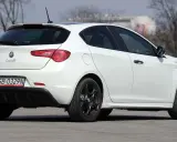 Biała Alfa Romeo Giulietta z czarnymi felgami stoi na asfalcie. Widoczny tył samochodu z tablicą rejestracyjną SB 0329N.
