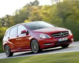 Czerwony Mercedes Klasy B w ruchu, z rozmytym tłem drzew i drogi.