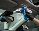 Ręka w czarnej rękawiczce czyści podsufitkę niebieską ściereczką i sprayem.