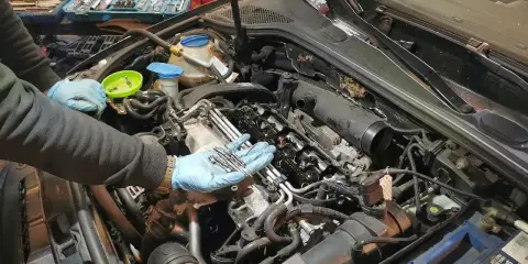 Mechanik w niebieskich rękawiczkach trzyma nowe świece żarowe, przygotowując się do ich wymiany w silniku samochodu.