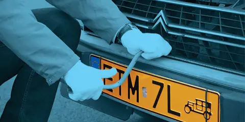 Ręce w białych rękawiczkach montują żółtą tablicę rejestracyjną z symbolem starego auta. Czy warto zarejestrować auto jako zabytek?