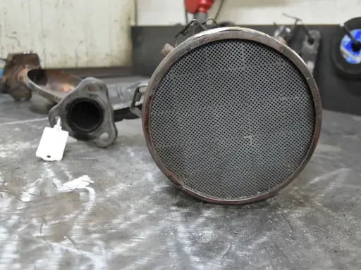 Zużyty filtr cząsteczek stałych, element układu wydechowego pojazdu, leży na metalowym blacie.