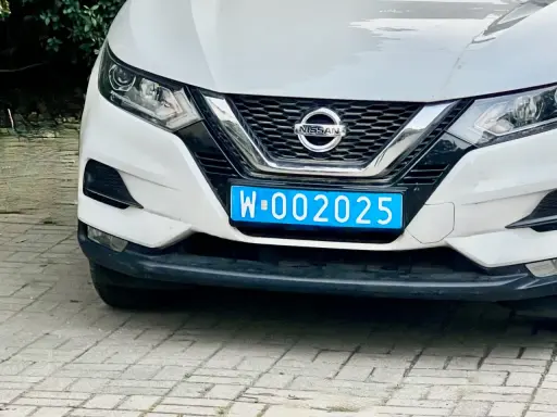 Biały Nissan z niebieską tablicą rejestracyjną W-002025, wskazującą na dyplomatyczne tablice rejestracyjne.