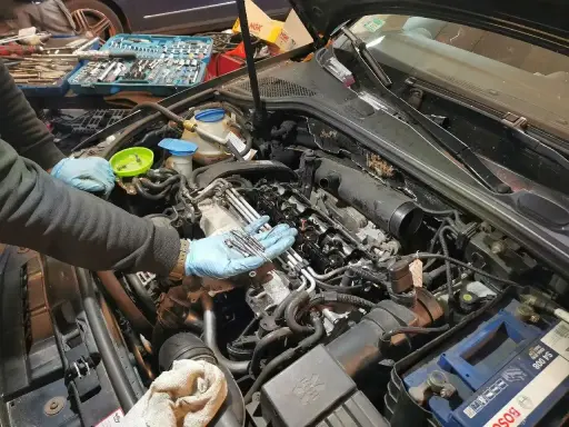 Mechanik w niebieskich rękawiczkach trzyma nowe świece żarowe, przygotowując się do ich wymiany w silniku samochodu.