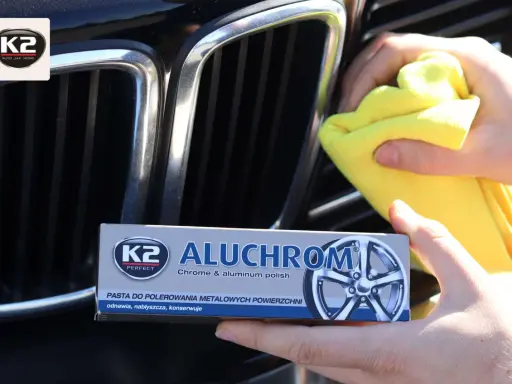 Ręce polerują chromowaną atrapę chłodnicy samochodu, używając żółtej ściereczki i pasty K2 Aluchrom.