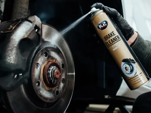 Ręka w czarnej rękawiczce rozpyla środek na zużyte tarcze hamulcowe. Preparat K2 Brake Cleaner skutecznie czyści hamulce.