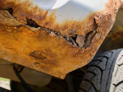 Widoczne zaawansowane ogniska rdzy na podwoziu samochodu, które doprowadziły do jego rozpadu. Obok widać fragment opony.