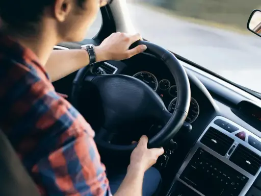 Mężczyzna w koszuli w kratę trzyma kierownicę, czując delikatne drgania kierownicy podczas jazdy.