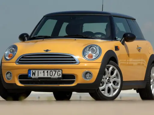Żółty Mini Cooper, jedna z nowszych generacji, z czarnym dachem i felgami.