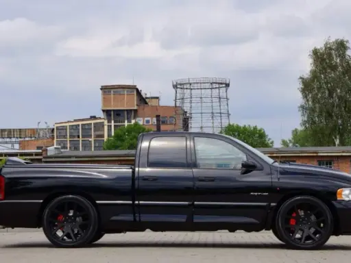 Czarny Dodge Ram 1500 SRT-10, potężny pickup, prezentuje swoje imponujące ramiona na tle postindustrialnego krajobrazu.
