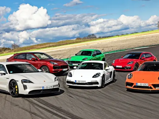 Różne rodzaje Porsche: biały Taycan, czerwony Cayenne, zielony Macan, biały Cayman, czerwona Panamera Sport Turismo i pomarańczowy 911 na torze wyścigowym.