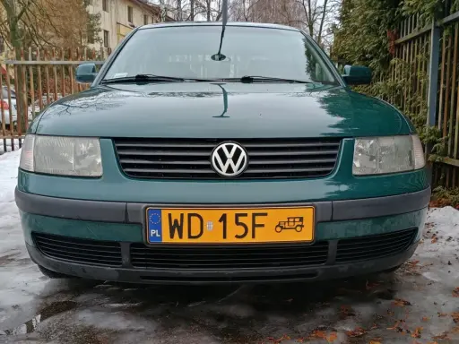Zielony Volkswagen z żółtą tablicą rejestracyjną na tle płotu i śniegu.