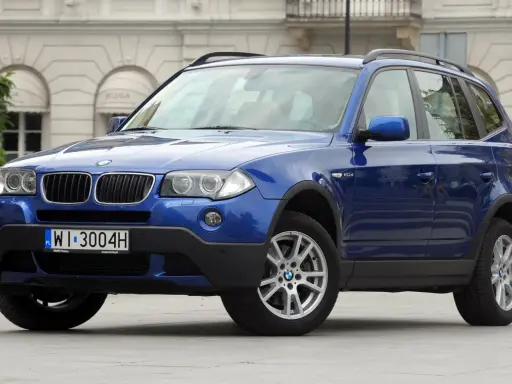 Niebieskie BMW E83, SUV, stoi przed budynkiem z łukami.