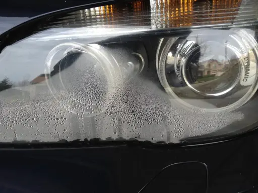 Zaparowany reflektor od środka, z licznymi kropelkami wody na kloszu.