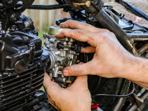 Ręce mechanika regulują gaźnik motocykla, pokazując, jak działa ssanie.