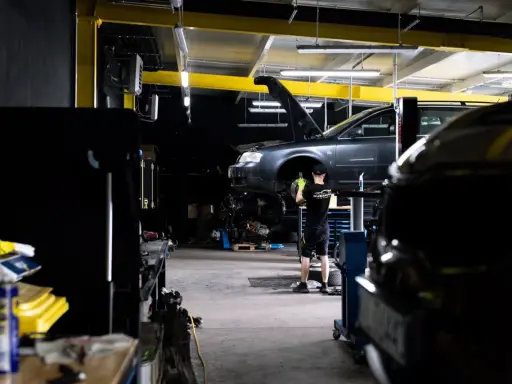 Mechanik bada przyczynę, dlaczego auto nie odpala. Podniesiony przód pojazdu i widoczny silnik sugerują skomplikowaną usterkę.