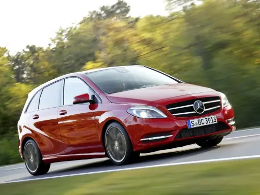 Czerwony Mercedes Klasy B w ruchu, z rozmytym tłem drzew i drogi.