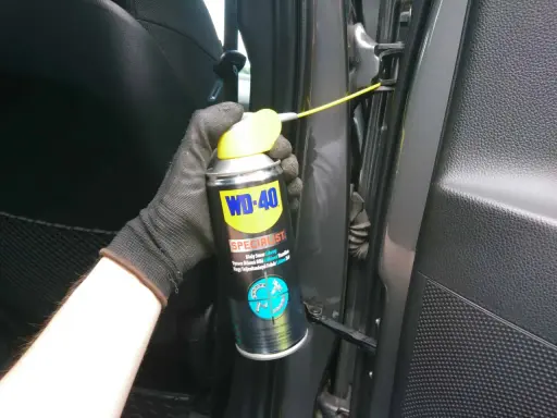Ręka w rękawiczce aplikuje smar do zawiasów drzwi samochodowych WD-40 Specialist.