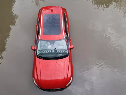 Czerwony samochód stoi w wodzie. Po powodzi czeka go osuszanie auta.