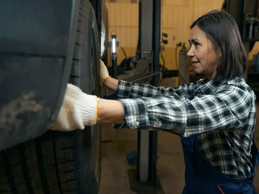 Mechaniczka w rękawiczkach sprawdza oponę, słysząc niepokojące stukanie w kole.