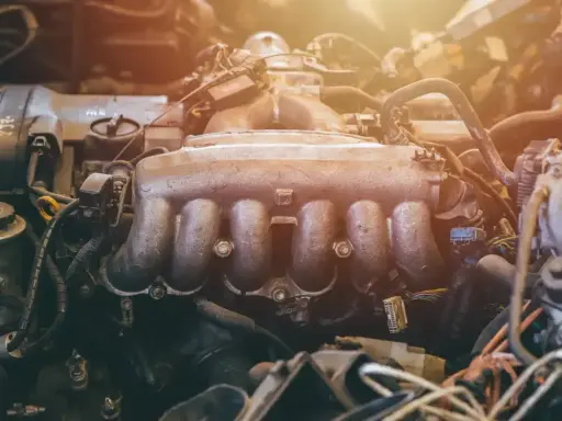 Silnik samochodowy z widocznym, zakurzonym kolektorem ssącym. Widać przewody i inne elementy mechaniczne.