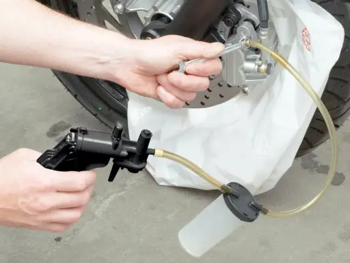 Ręce majsterkowicza odkręcają odpowietrznik zacisku hamulcowego, przygotowując się do tego, jak wymienić płyn hamulcowy w motocyklu.