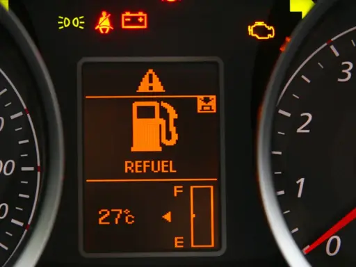 Na desce rozdzielczej świeci się kontrolka paliwa z napisem "REFUEL". Wskaźnik pokazuje niski poziom paliwa, sugerując, że rezerwa ile km zostało do przejechania jest niewielka.