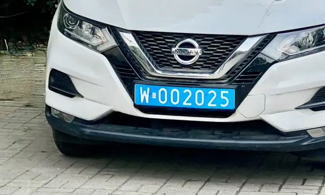 Biały Nissan z niebieską tablicą rejestracyjną W-002025, wskazującą na dyplomatyczne tablice rejestracyjne.