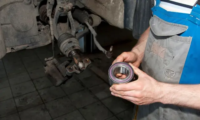 Mechanik trzyma nowe łożysko koła, przygotowując się do wymiany. Tak sprawdzić łożysko w kole.