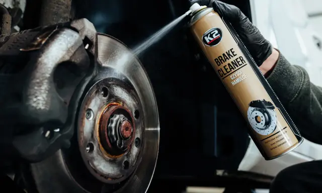Ręka w czarnej rękawiczce rozpyla środek na zużyte tarcze hamulcowe. Preparat K2 Brake Cleaner skutecznie czyści hamulce.