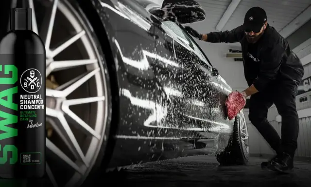 Mężczyzna myje czarne auto pianą, używając gąbki. Obok butelka szamponu SWAG.