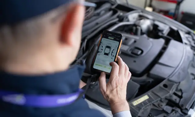 Mechanik sprawdza kody samochodowe na telefonie, analizując raport z pomiaru lakieru i szczelin.