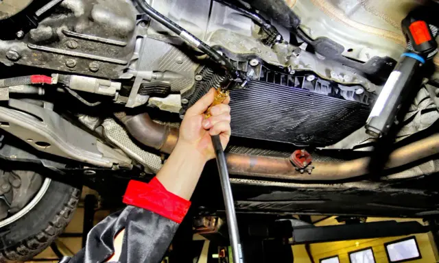 Mechanik wykonuje wymianę oleju w skrzyni automatycznej, używając specjalistycznego sprzętu do serwisu.