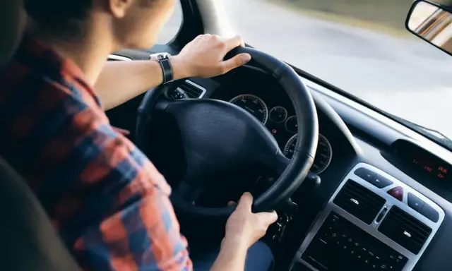 Mężczyzna w koszuli w kratę trzyma kierownicę, czując delikatne drgania kierownicy podczas jazdy.